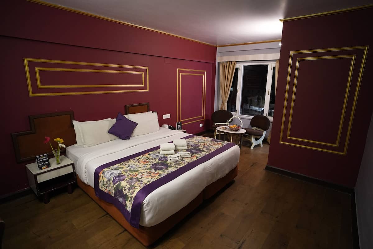 A hotel room with a large bed, a nightstand with a vase of flowers, and a window with curtains.