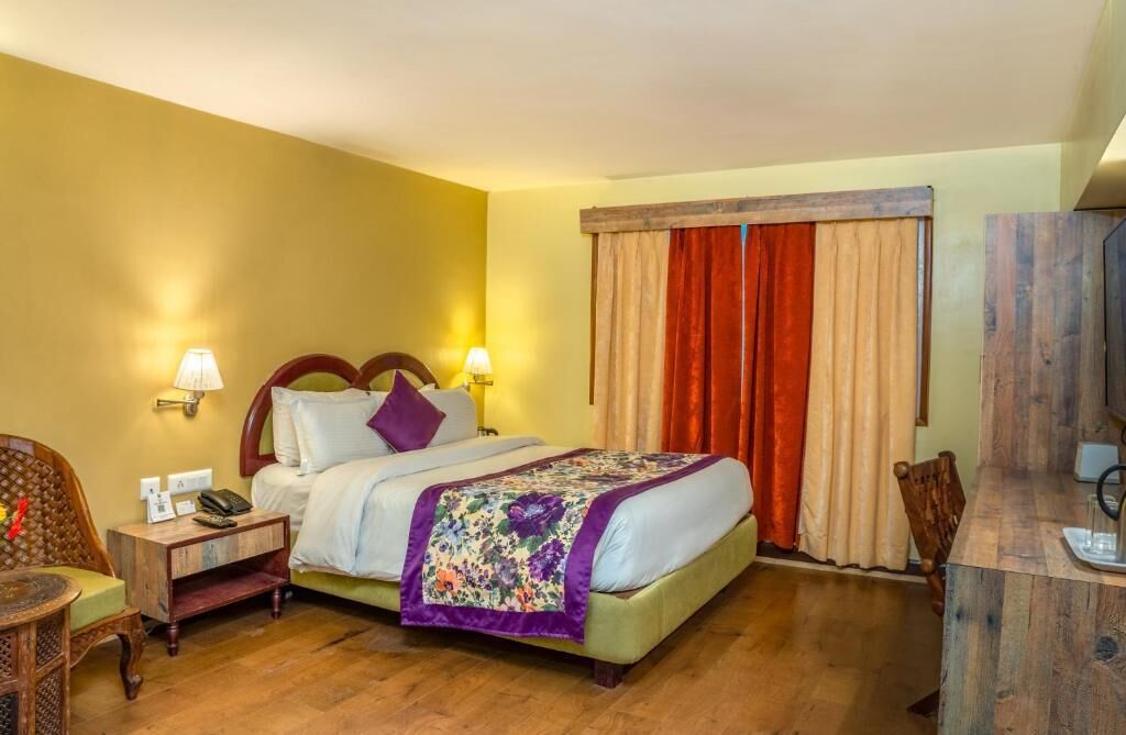 A hotel room with a bed, bedside lamps, a wooden nightstand, a chair, and a desk with a mirror.