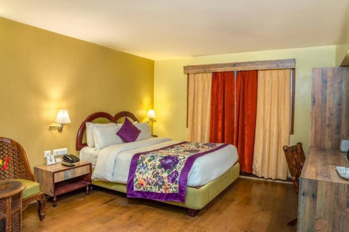 A hotel room with a bed, bedside lamps, a wooden nightstand, a chair, and a desk with a mirror.