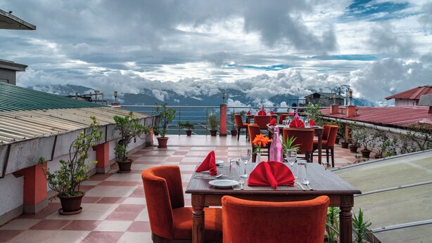 Un restaurante al aire libre con mesas preparadas para comer, plantas en macetas y vistas a montañas.