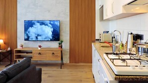 Moderni keittiö, jossa on sisäänrakennettu liesi, mikroaaltouuni ja kaapistot. Seinälle on asennettu litteänäyttöinen televisio, ja sen alapuolella on puinen konsolipöytä, jonka päällä on kasvi.
