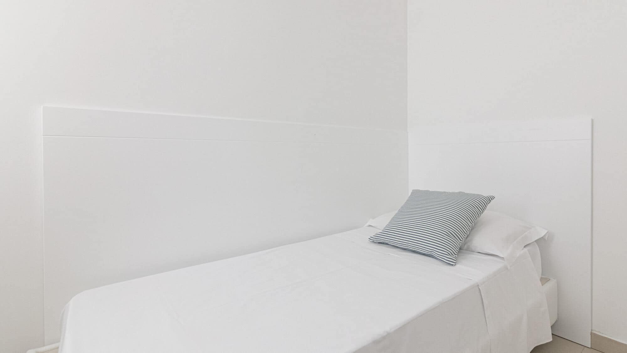 A small, single-bed room with a plain white headboard and a striped pillow.