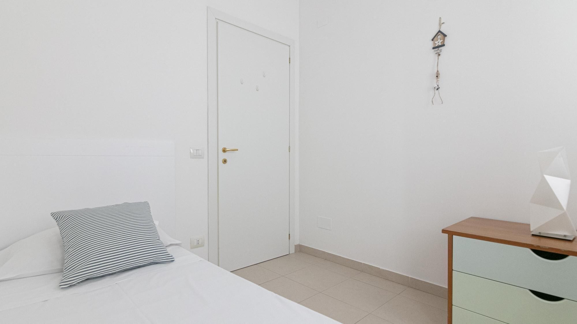 A minimalist bedroom with a bed, a bedside table, and a door.