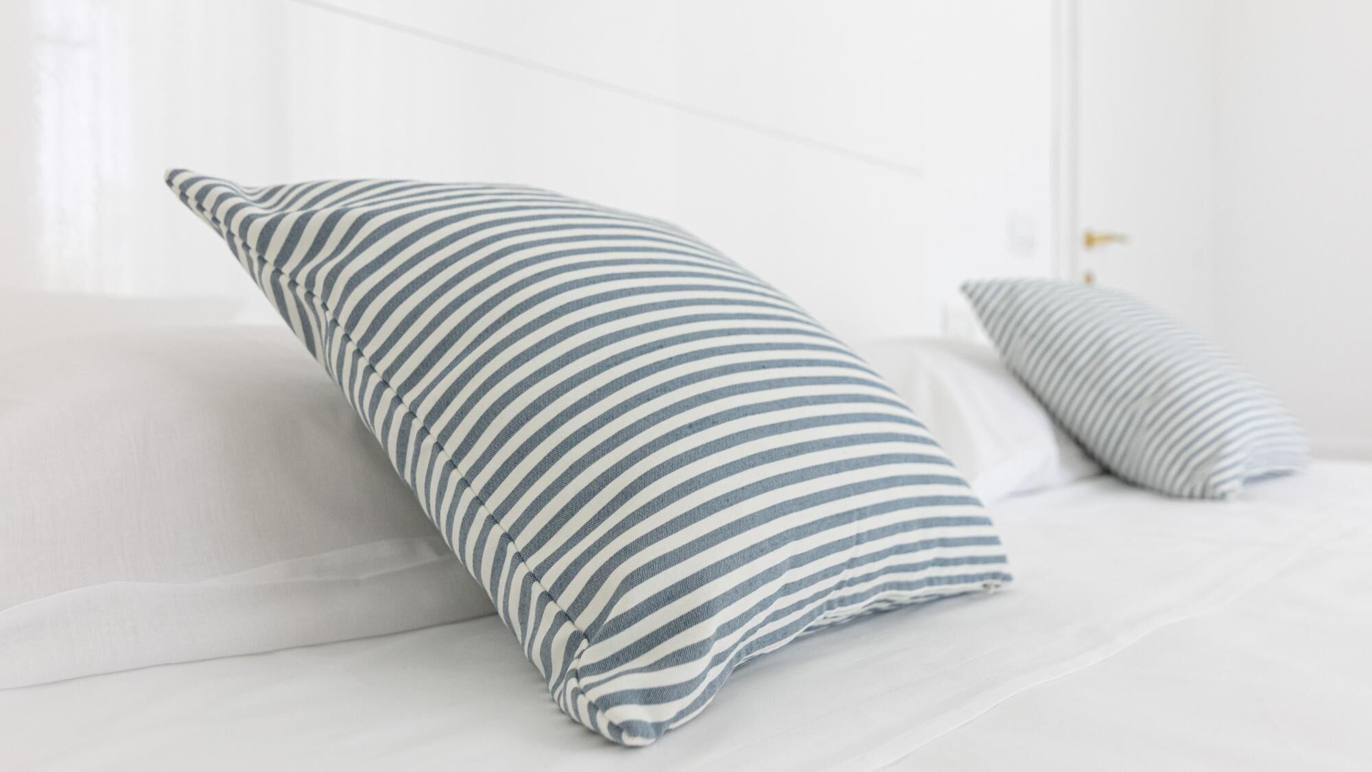 A bed with two pillows, one striped and one solid, in a bright room.