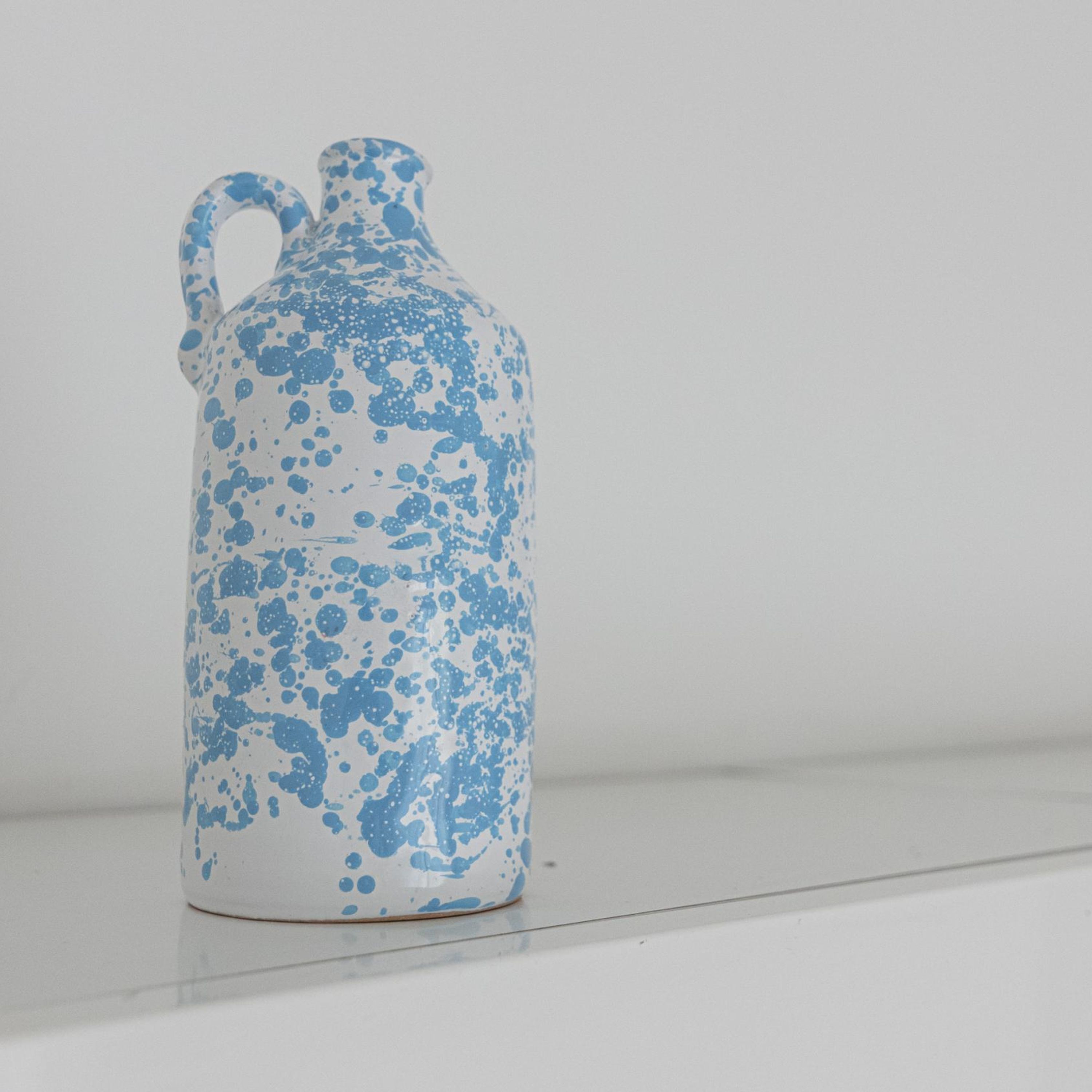 A white ceramic jug with blue splatter patterns and a handle, placed on a white surface.