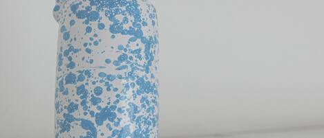 A white ceramic jug with blue splatter patterns and a handle, placed on a white surface.