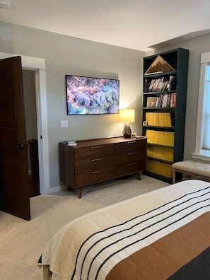 Ein Schlafzimmer mit Bett, Kommode, Bücherregal und Fernseher an der Wand.