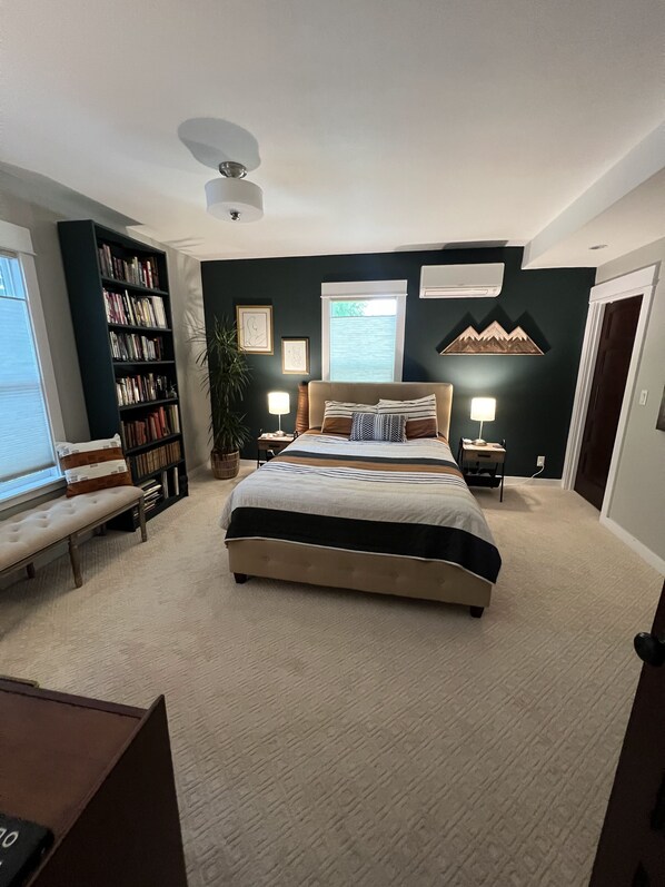 Um quarto com uma cama grande, uma estante, uma escrivaninha e uma janela.