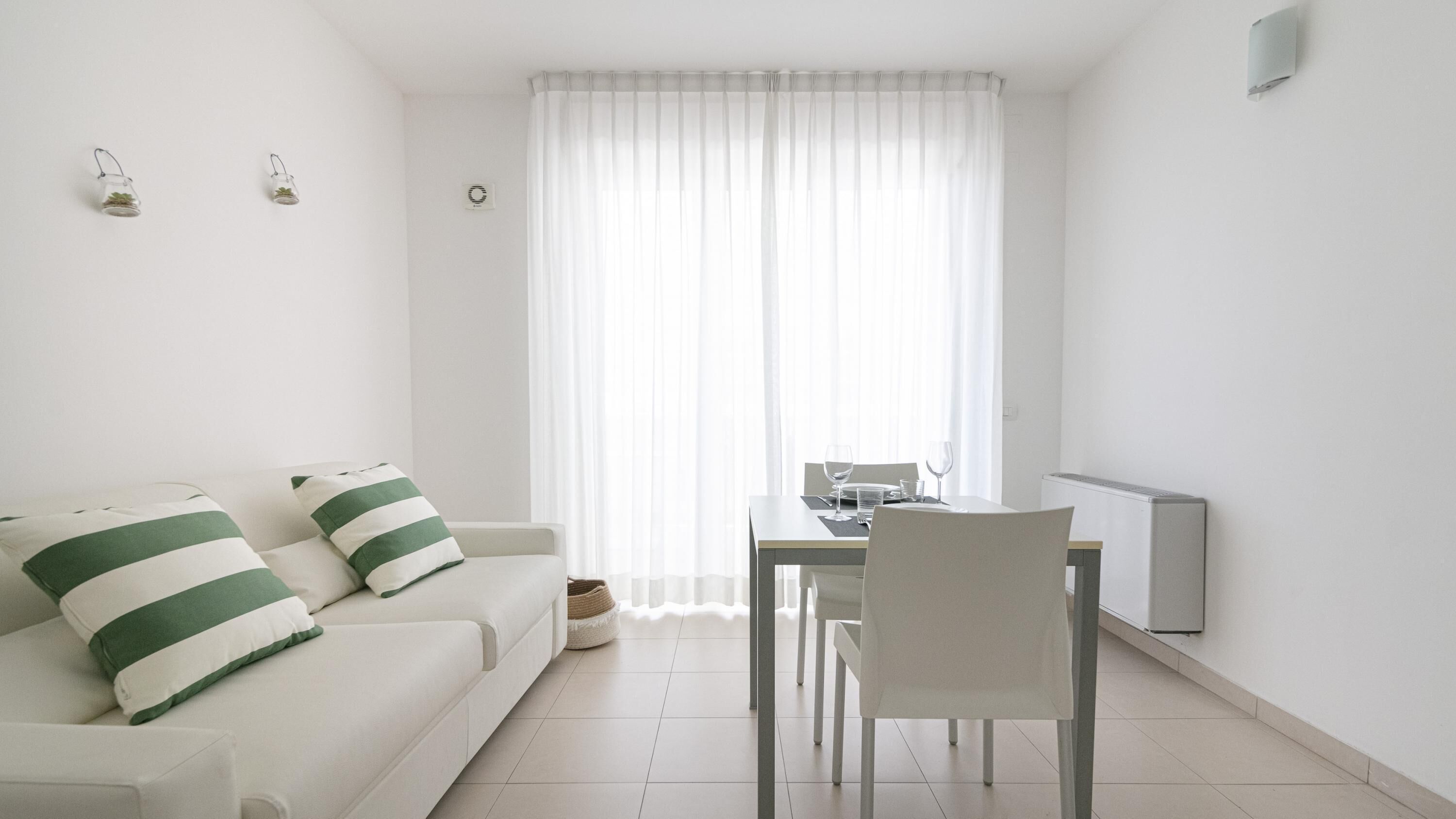 A modern, minimalistic living room with a white sofa, a dining table, and a chair.