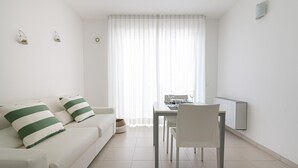 Un salón moderno y minimalista con un sofá blanco, una mesa de comedor y una silla.