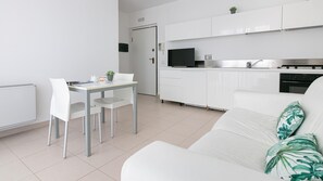 Une cuisine moderne avec des meubles blancs, une table à manger avec des chaises, un canapé blanc avec un coussin vert et une petite plante en pot posée sur le comptoir.