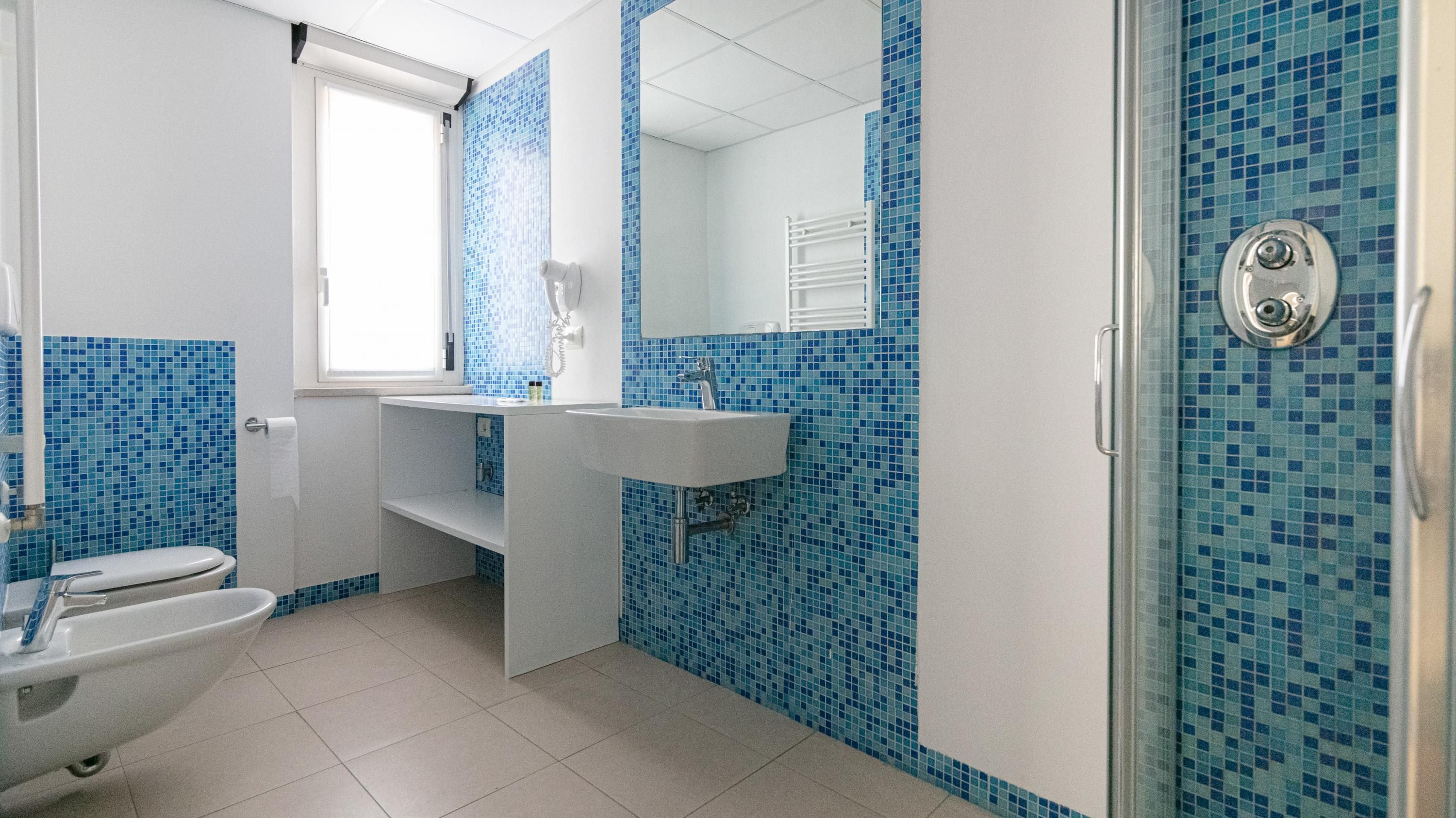 A bathroom with a toilet, sink, and shower area, featuring blue mosaic tiles.