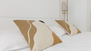 Un lit avec deux oreillers et une lampe fixée au mur.