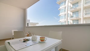En balkon med et bord, stole, et vindue og en bygning i baggrunden.