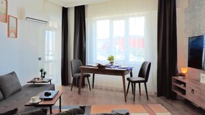 Een moderne woonkamer met een bank, een eettafel met stoelen, een televisie en een groot raam met gordijnen.