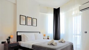 Een moderne hotelkamer met een groot bed, een nachtkastje, een lamp en een raam met dunne gordijnen.