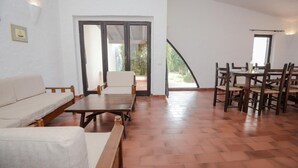 A spacious living area with a sofa, a wooden table, and a dining set. There is a sliding glass door leading to an outdoor area. - Villa Chiara in Costa Rei (Muravera)