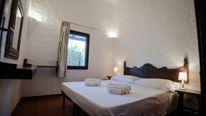 A bedroom with a large bed, two bedside tables with lamps, a window with curtains, and a textured wall. - Villa Chiara in Costa Rei (Muravera)