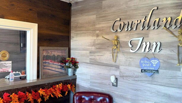 A reception area with a wooden wall, a sign reading "Courtland Inn," a heart-shaped sign with a WiFi password, and a red leather chair. - Courtland Inn By Townhouse Franklin VA US 58 (Courtland)