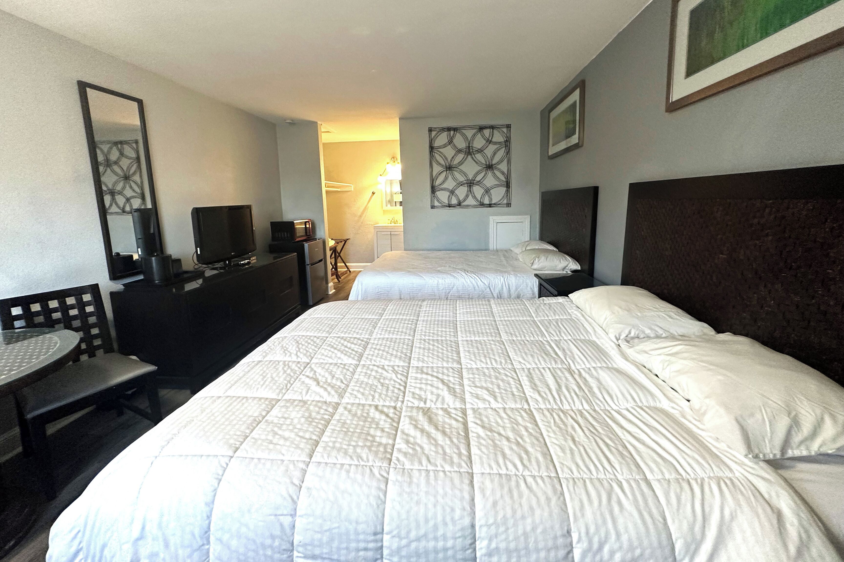 A hotel room with a large bed, a desk with a chair, a TV, and a mirror.