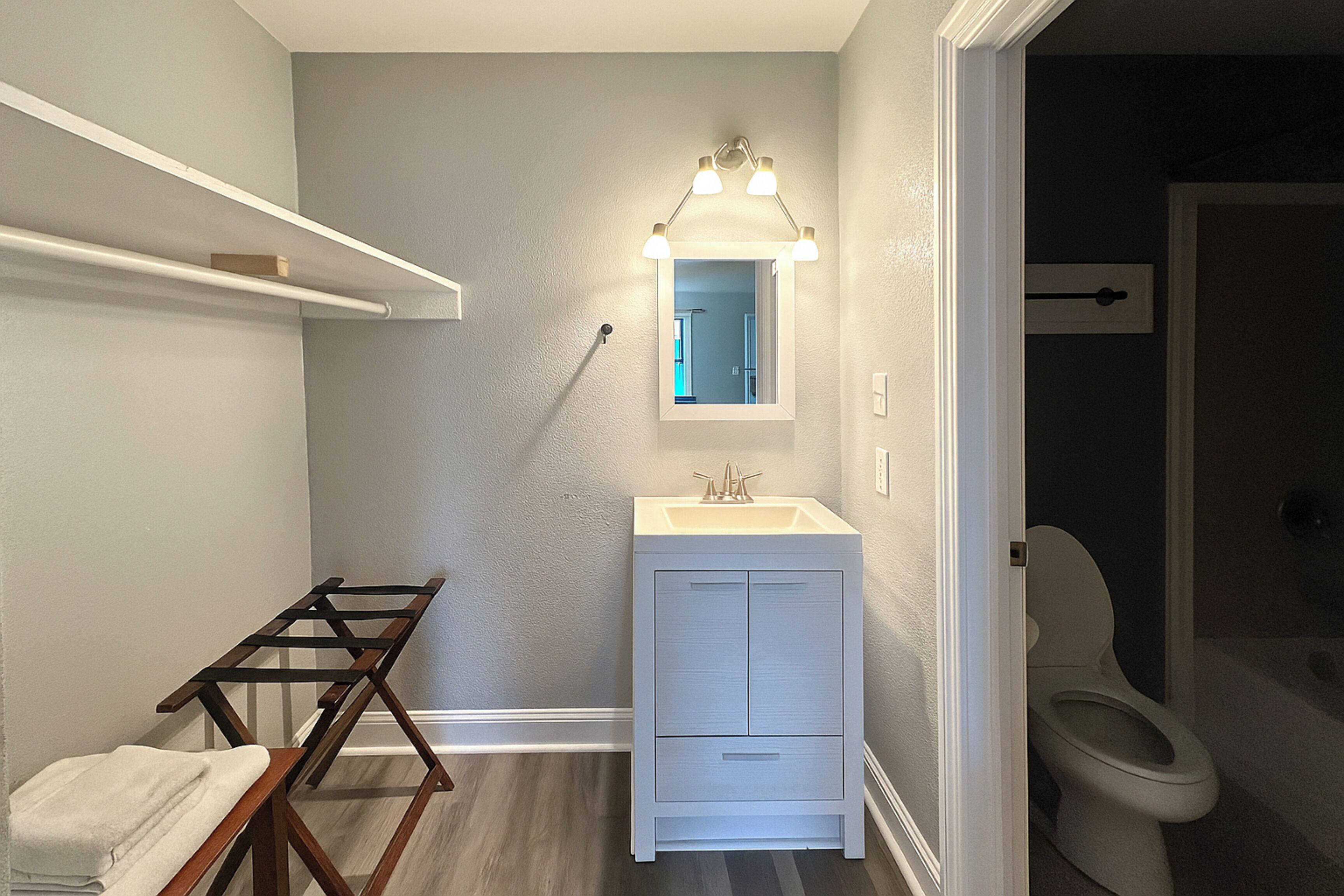 Uma casa de banho com lavatório branco, espelho iluminado, porta-toalhas e sanita.