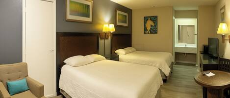 A hotel room with two beds, a chair, a small table, and a TV.