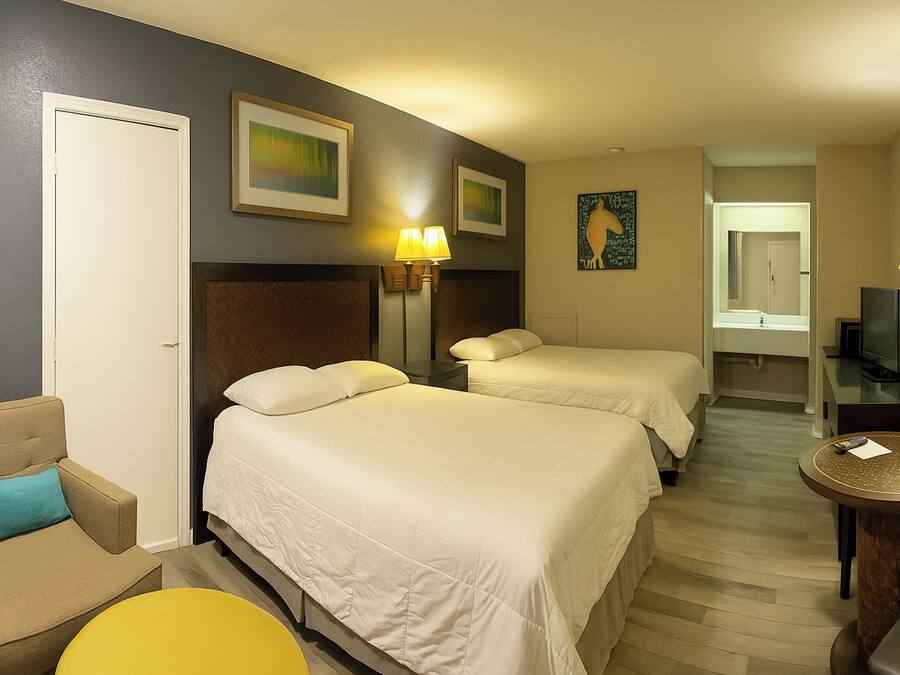 Habitación de hotel con dos camas, una silla, una mesita pequeña y un televisor.