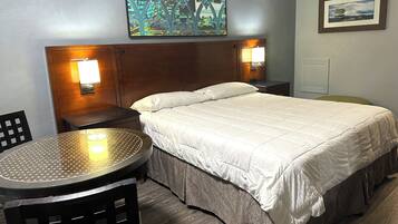 A hotel room with a bed, two bedside lamps, a round table with a chair, and artwork on the walls.