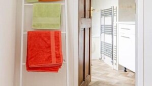 Um corredor com um porta-toalhas branco com três toalhas, uma porta de madeira e vista para um quarto com varanda.