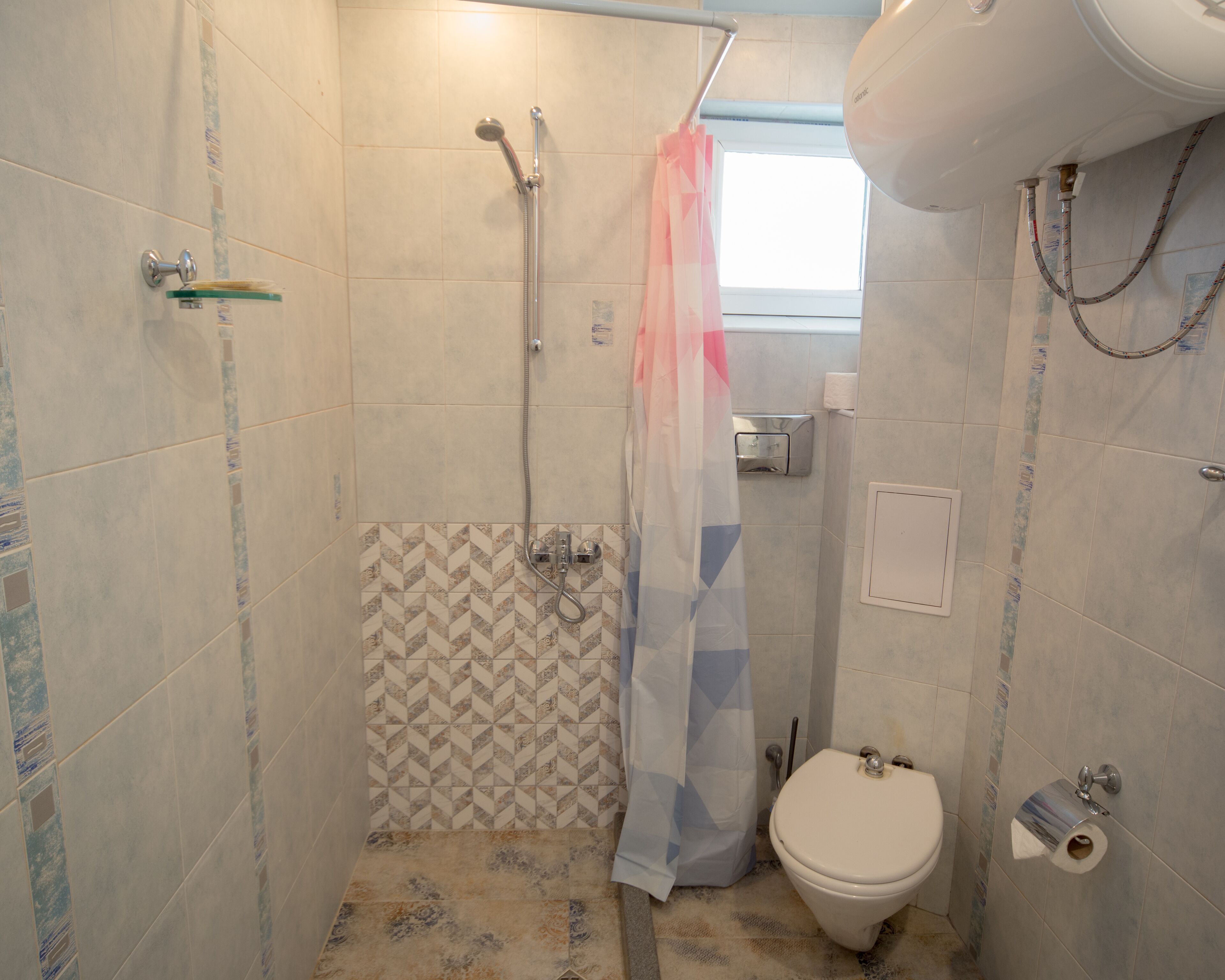 A small bathroom with a shower, toilet, and a window.
