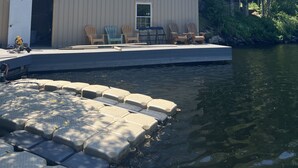 A lakeside cabin with a dock, outdoor seating, and a large glass window overlooking the water. - STUNNING LARGE CHALET COTTAGE IN MUSKOKA (Coldwater)