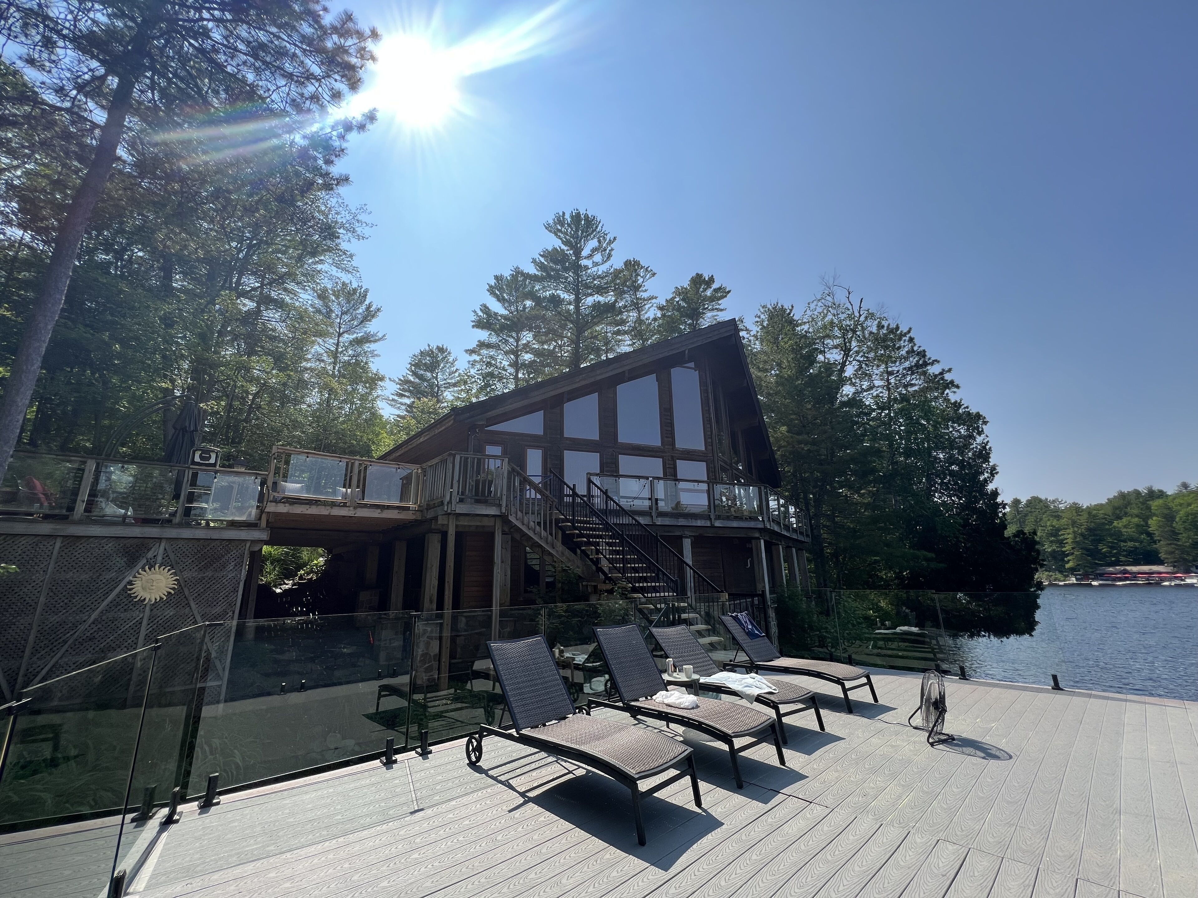 Een houten terras met lounge fauteuils, een glazen balustrade en uitzicht op een meer.