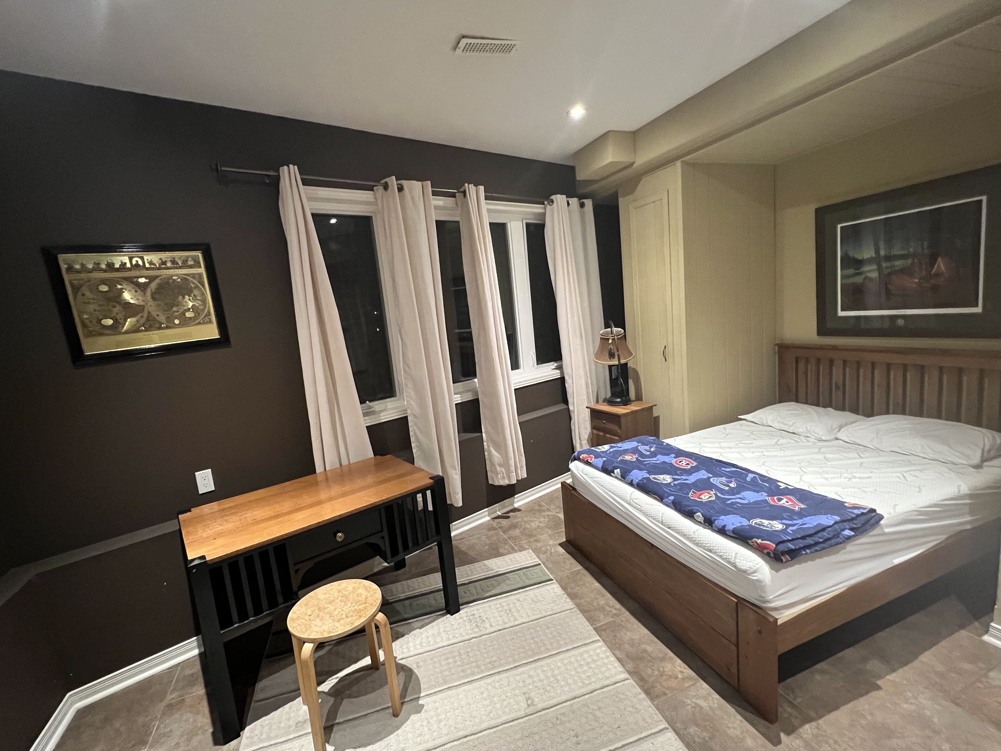 A bedroom with a bed, a desk, a chair, a lamp, and a window with curtains.
