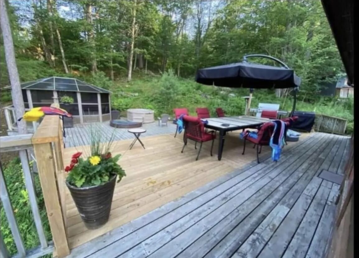 Eine Holzterrasse mit Gartenmöbeln, darunter ein Tisch und Stühle, sowie ein überdachter Bereich mit Grill.