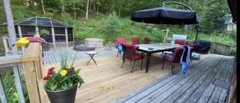 Una terraza de madera con mobiliario exterior, incluyendo una mesa y sillas, y una zona cubierta con una parrilla.