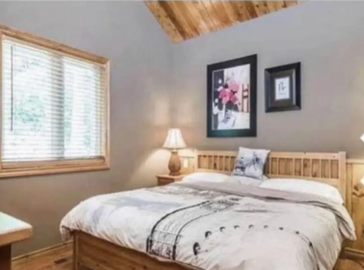 Ein Schlafzimmer mit hölzernem Kopfteil, einem Bett mit gemustertem Bettbezug, einem Nachttisch mit Lampe und zwei gerahmten Bildern an der Wand.
