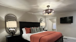 A bedroom with a large bed, two bedside tables, a mirror, a ceiling fan, and a TV on the wall.