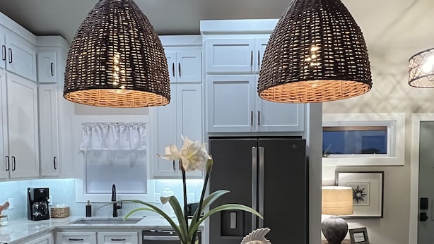 A modern kitchen with white cabinets, a central island with a vase of flowers, and two hanging wicker pendant lights.