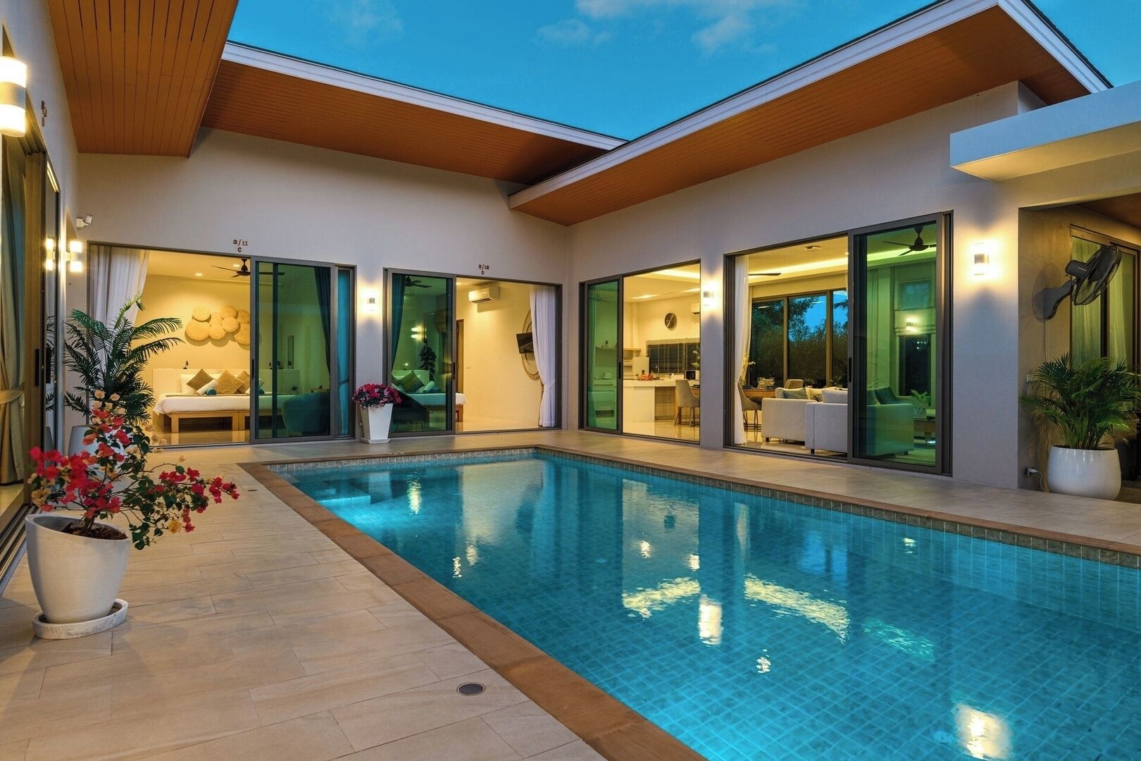 Uma casa moderna com piscina, grandes portas de vidro que dão para uma sala de jantar e interior bem iluminado.