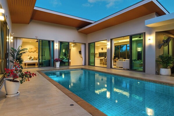 A modern house with a swimming pool, large glass doors leading to a dining area, and a well-lit interior.