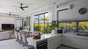 A modern kitchen with a dishwasher, a microwave, and a sink. There is a dining area with a table and chairs, and a large window with a view of greenery.