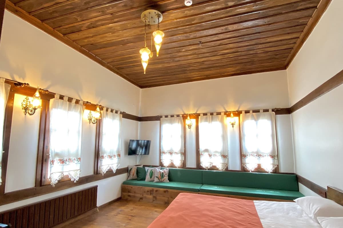 A room with a wooden ceiling, a bed with a red blanket, a green bench, and a television on the wall.