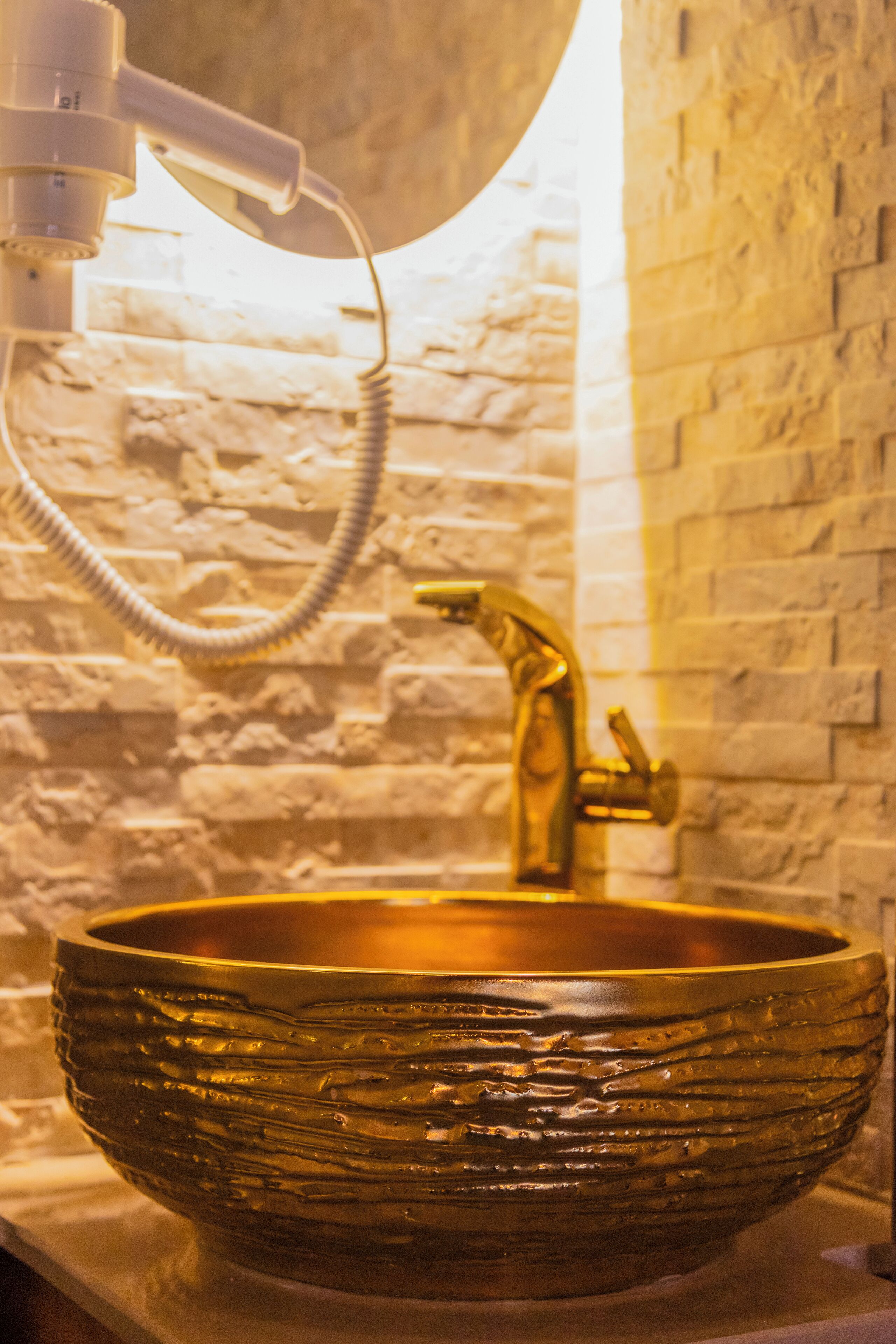 Lavabo dorato con rubinetto curvo in un bagno con parete in pietra.