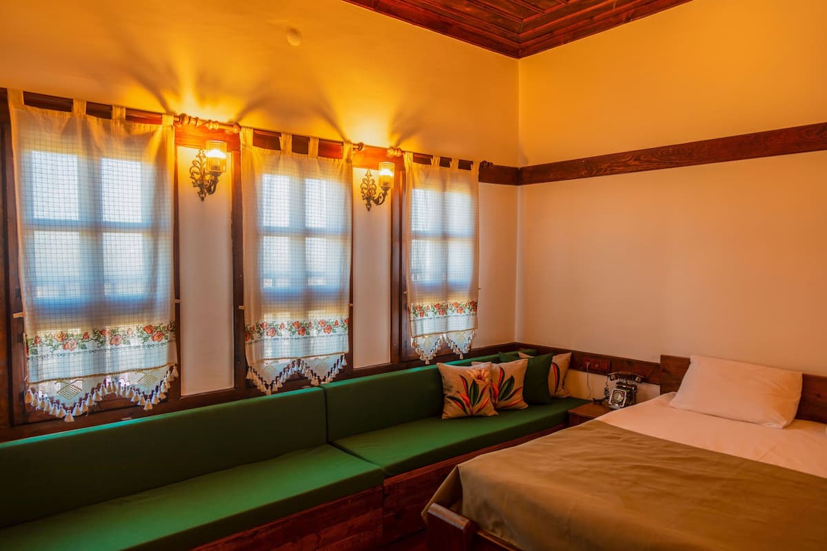 A room with a green sofa, a bed, and a window with curtains.