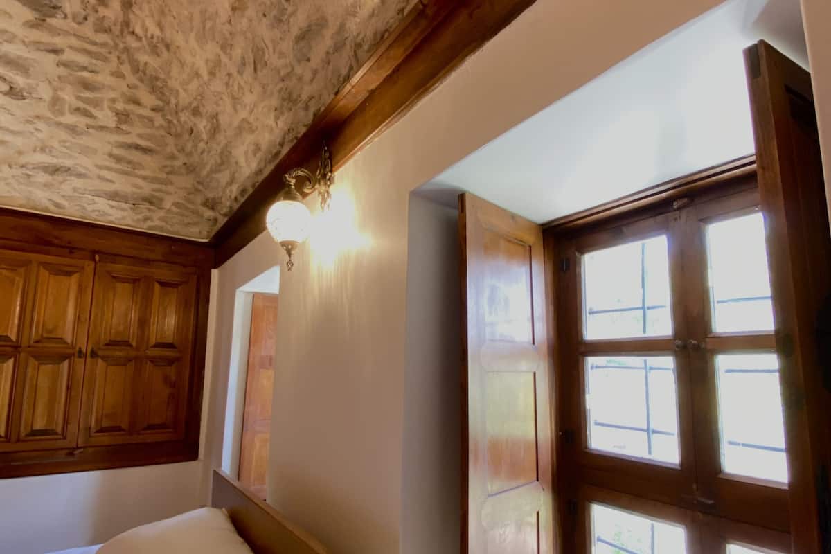 A bedroom with a stone ceiling, wooden headboard, and a large window with multiple panes.