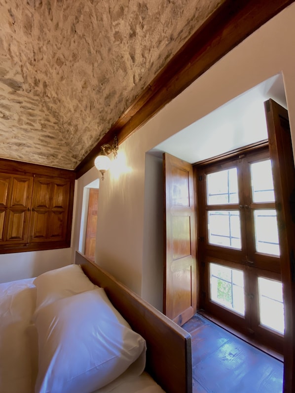 Quarto com teto de pedra, cabeceira de madeira e uma grande janela com vários painéis.