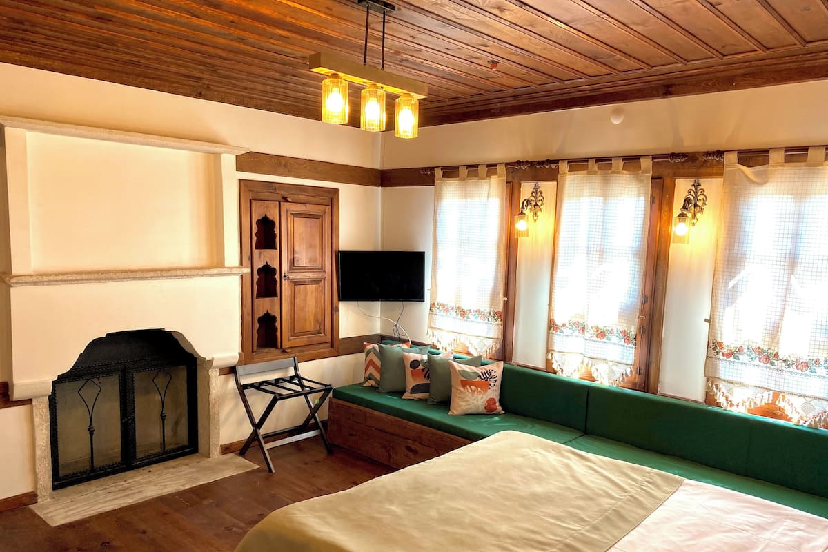 A room with a bed, a wooden ceiling, a fireplace, a TV, and a window with curtains.