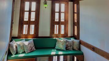 Une pièce avec un plafond en bois, un banc vert rembourré agrémenté de coussins décoratifs et une table en verre.