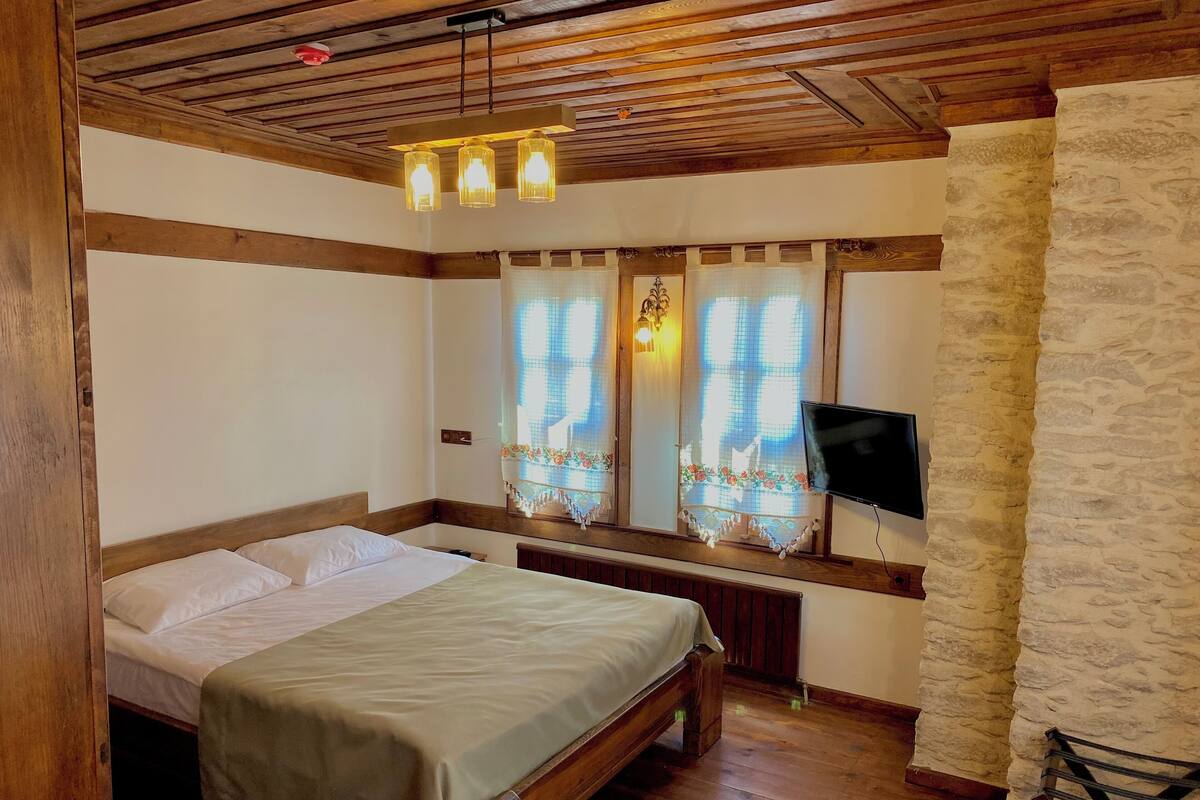 A bedroom with a wooden bed, a television mounted on the wall, and a stone accent wall.