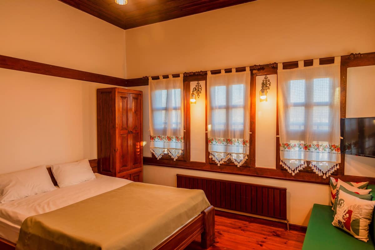 A bedroom with a bed, a wooden wardrobe, a radiator, and a window with lace curtains.